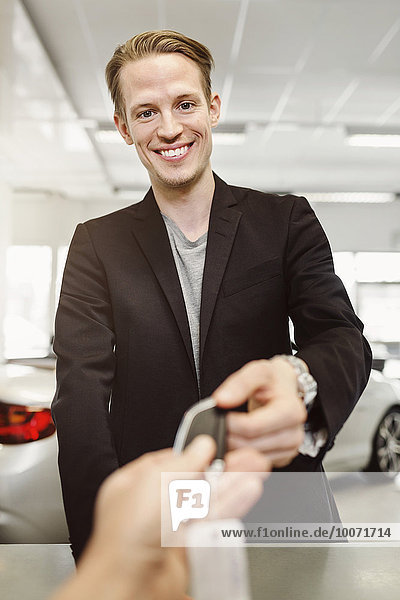 Portrait of happy man receiving keys from saleswoman in car dealership