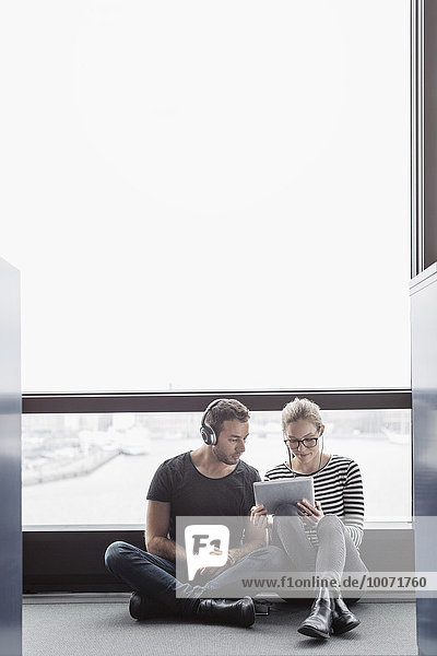 Geschäftskollegen  die im Büro am Fenster sitzen und ein digitales Tablett benutzen