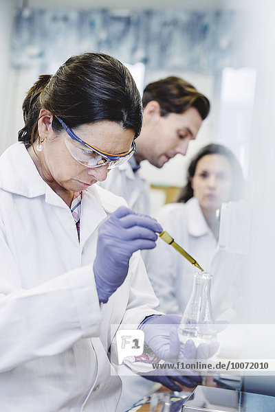 Wissenschaftlerin untersucht Probe im Labor mit Kollegen im Hintergrund
