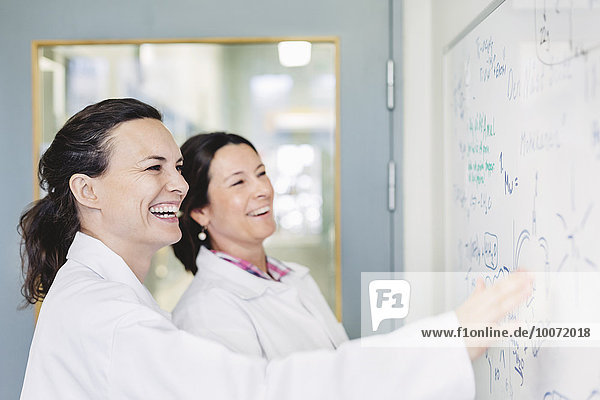 Happy female scientists discussing plan on whiteboard in laboratory