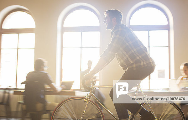 Lässiger Geschäftsmann auf dem Fahrrad im sonnigen Büro