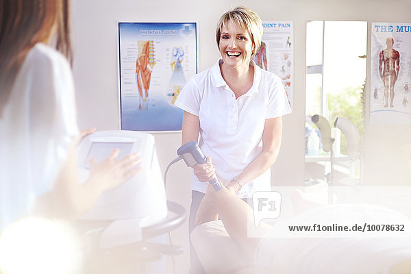 Lächelnder Physiotherapeut mit Ultraschallsonde am Bein des Patienten