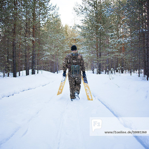 Caucasian man carrying skis on snowy road