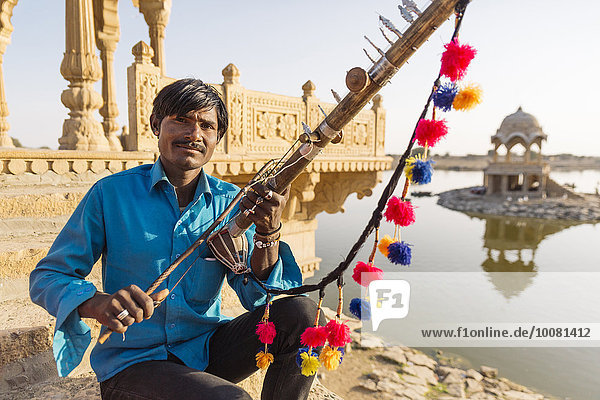 Indian man holding traditional instrument near monument  Jaisalmer  Rajasthan  India