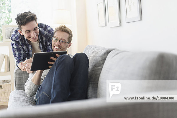 Caucasian gay couple using digital tablet on sofa