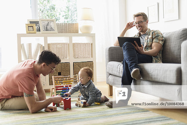Caucasian gay fathers and baby relaxing in living room