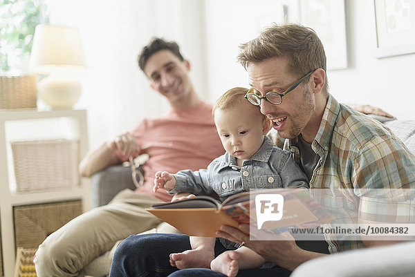 Caucasian gay fathers reading to baby in living room