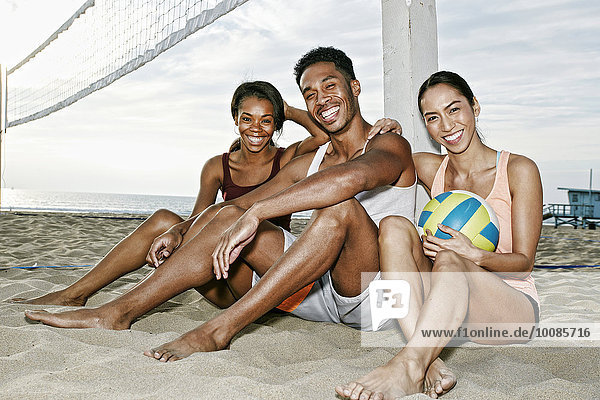 Friends sitting near volleyball net on beach
