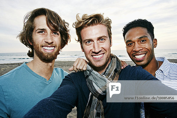 Smiling men taking selfie on beach