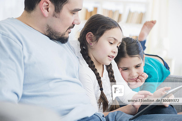 Caucasian father and daughters using digital tablet on sofa