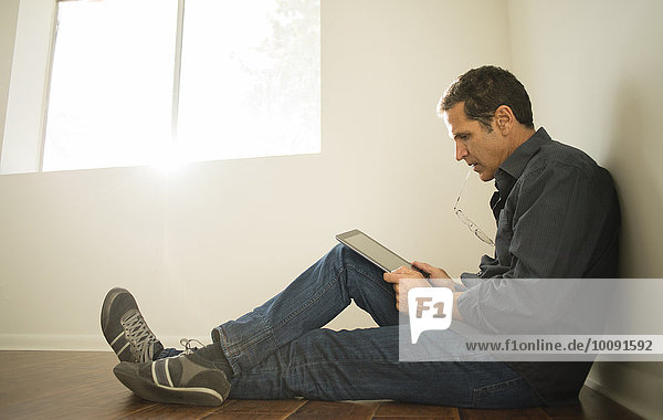 Hispanic man using digital tablet on floor of empty room