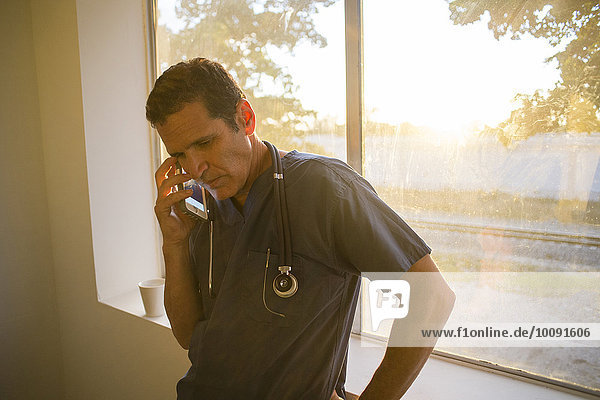 Hispanic doctor talking on cell phone at window
