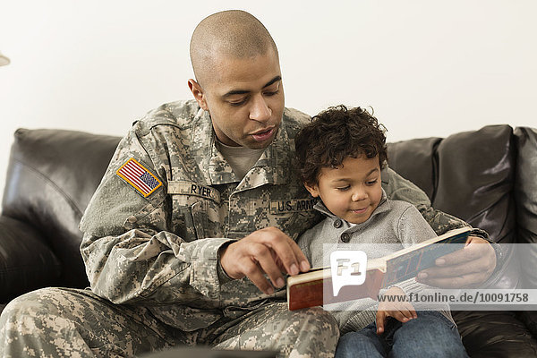Mixed race soldier reading book to son on sofa