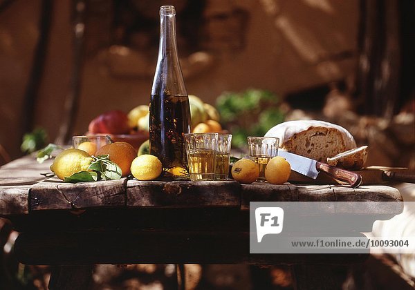 Holztisch mit Öl  Gläsern  Brot und Zitronen im Freien