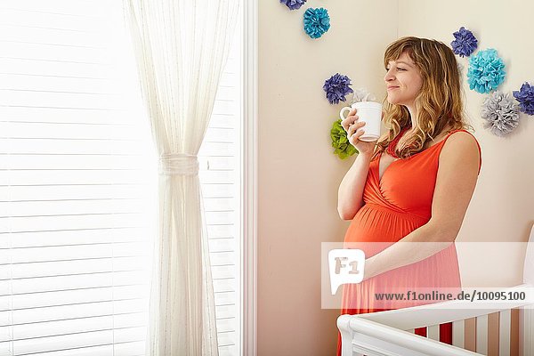 Schwangere Frau trinkt Kaffee und träumt im Kinderzimmer