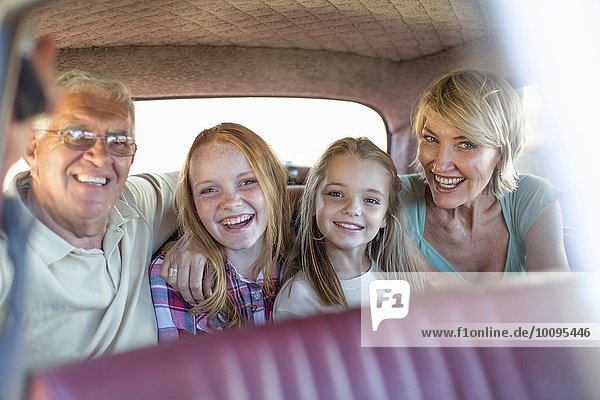 Großeltern und Enkelkinder sitzen auf dem Rücksitz des Autos und lächeln.