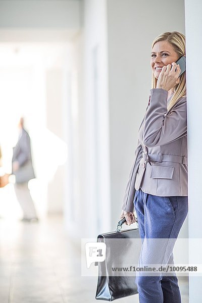Mittlere erwachsene Geschäftsfrau beim Plaudern auf dem Smartphone im Hotelkorridor