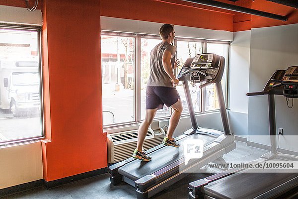 Exhausted mid adult man running uphill on gym treadmill