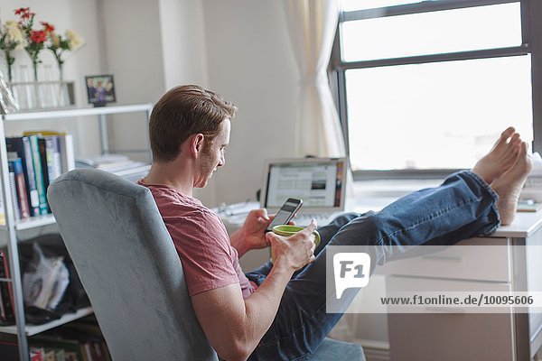 Mid Erwachsene Mann mit Füßen auf dem Schreibtisch lesen Smartphone-Texte