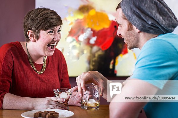 Mid adult man and young woman laughing and drinking in recreational bar