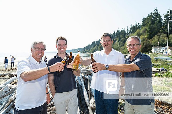 Portrait of mature men and son toasting each other with bottled beer on beach