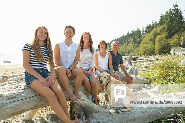 Portrait of mature parents  three daughters with dog sitting on beached tree