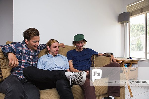 Drei junge Männer sitzen auf dem Sofa und schauen auf das Smartphone.