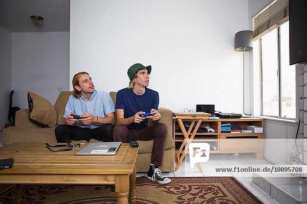 Two young men sitting on sofa  playing video game