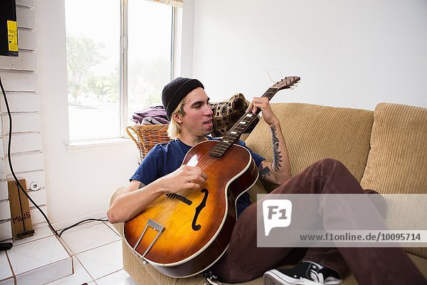 Junger Mann sitzt auf dem Sofa und spielt Gitarre.