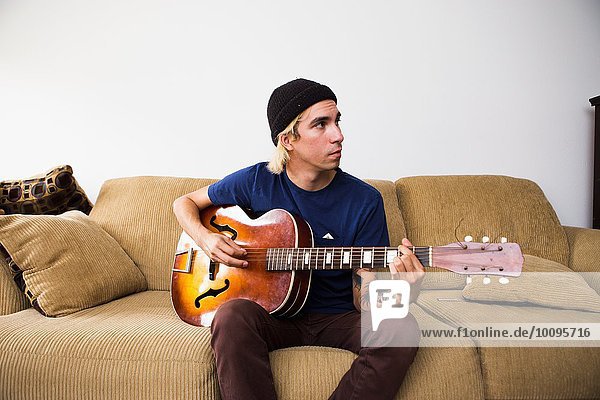 Young man sitting on sofa  playing guitar