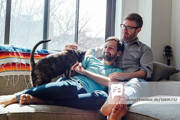 Männliches Paar entspannt sich mit Katze auf dem Sofa