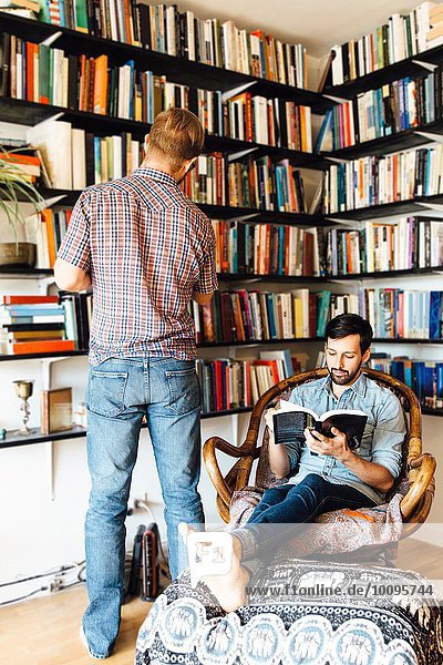 Male couple at home  reading and looking at books on bookshelf