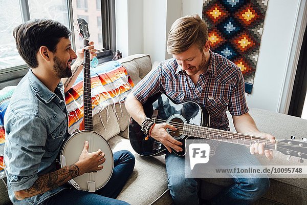Male couple at home  play guitar and banjo  laughing