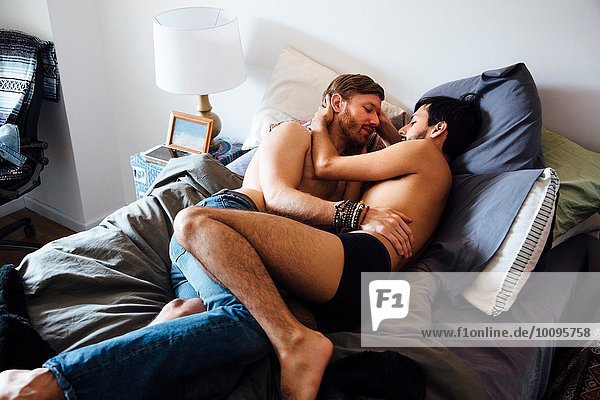 Male couple  partially dressed  lying on bed  embracing