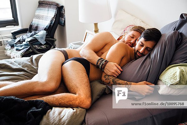 Male couple  partially dressed  lying together on bed  sleeping