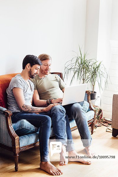 Male couple sitting on sofa  looking at laptop