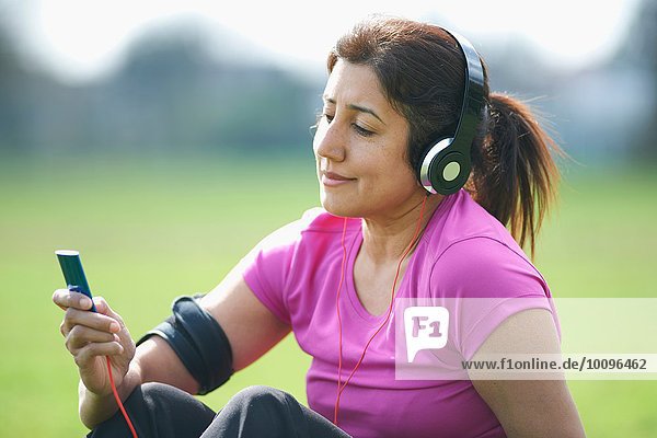 Reife Frau beim Sport im Park  Musik vom MP3-Player auswählen