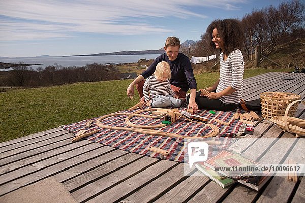 Boy and parents playing with toy train on wooden decking
