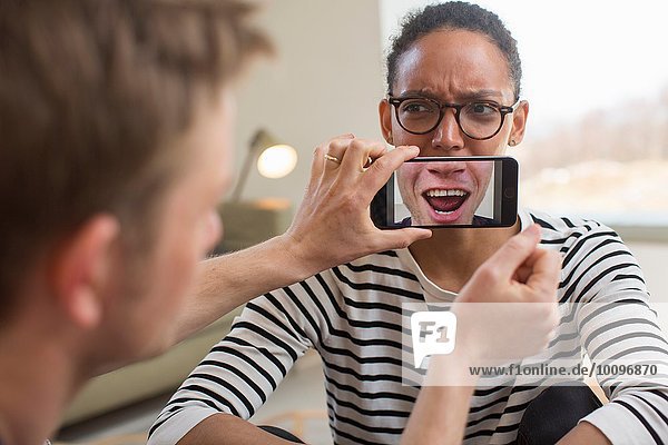Mann hält Smartphone vor den Mund der Frau
