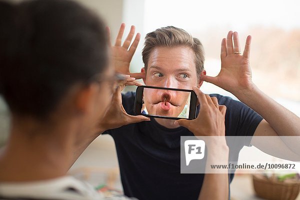 Woman holding smartphone in front of man's mouth