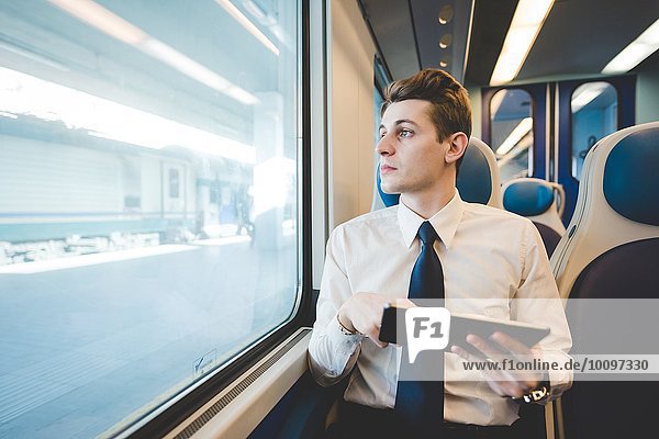 Porträt eines jungen Geschäftsmannes  der mit einem digitalen Tablett im Zug unterwegs ist.