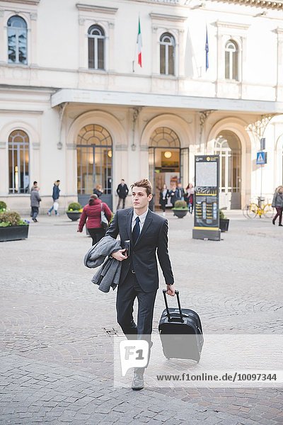 Junger Geschäftsmann  der mit dem Koffer die Kopfsteinpflasterstraße entlanggeht.