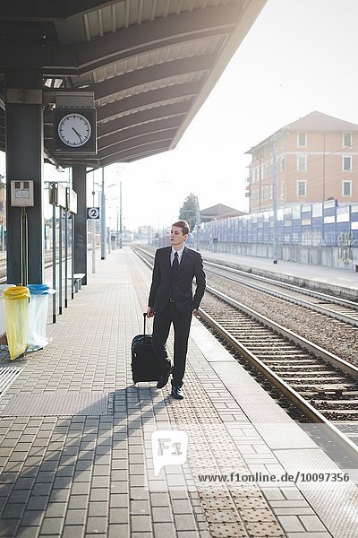 Portrait of young businessman commuter walking along railway platform.