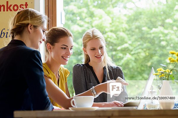 Three young women pointing at laptop in cafe