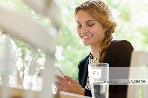 Junge Frau im Café beim Lesen von Texten auf dem Smartphone