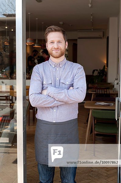 Portrait of proud young male cafe owner in doorway