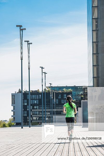 Rear view of mature female runner running in city