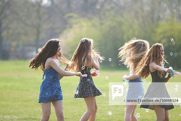 Vier Teenagermädchen beim Blasenspinnen mit Blasenstab im Park