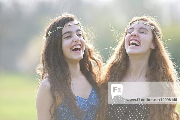 Zwei Teenager-Mädchen in Gänseblümchen-Kopfbedeckung lachend im Park