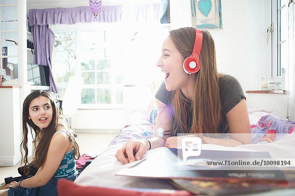 Teenagermädchen im Gespräch mit einem Freund  während sie Kopfhörer im Schlafzimmer hören.